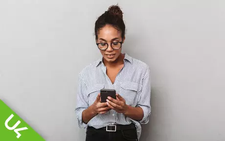 Woman, smiling and looking down at mobile phone, which she is holding in both hands